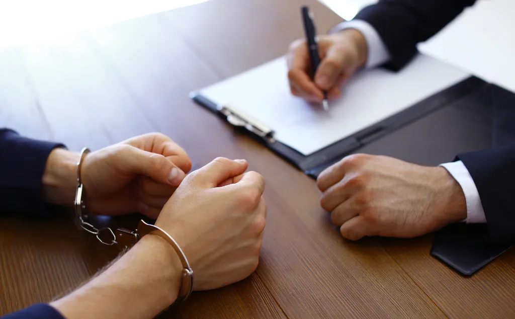 Police officer interrogating criminal in handcuffs at desk indoors