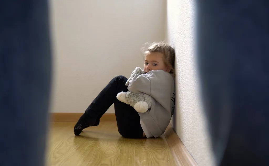 Child abuse concept. Mistreated little girl seating on the floor and scared of adult.