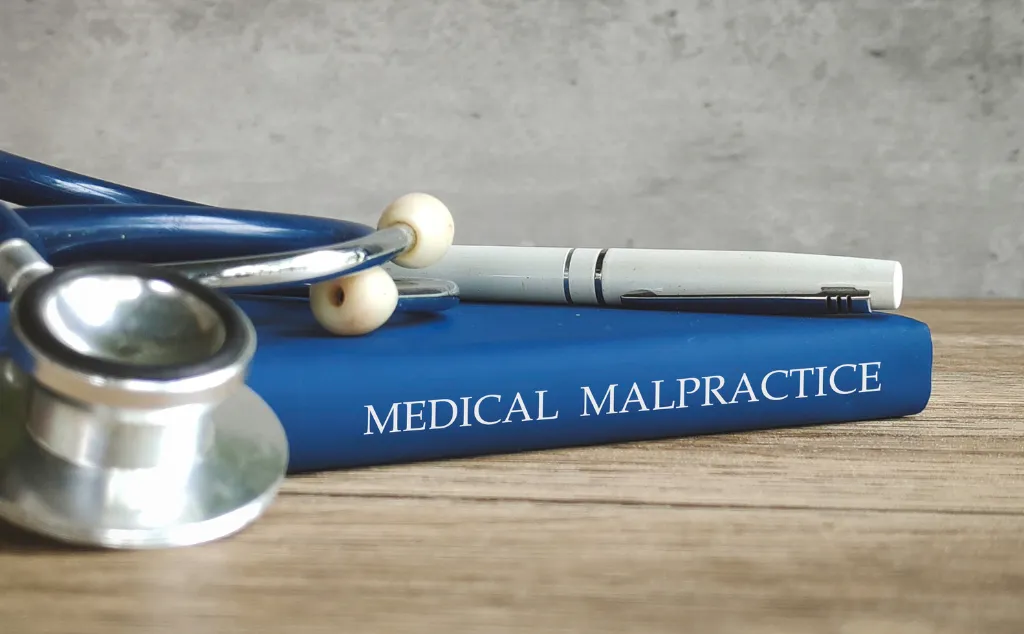 Stethoscope and a pen on a book titled "MEDICAL MALPRACTICE," representing legal issues in healthcare.