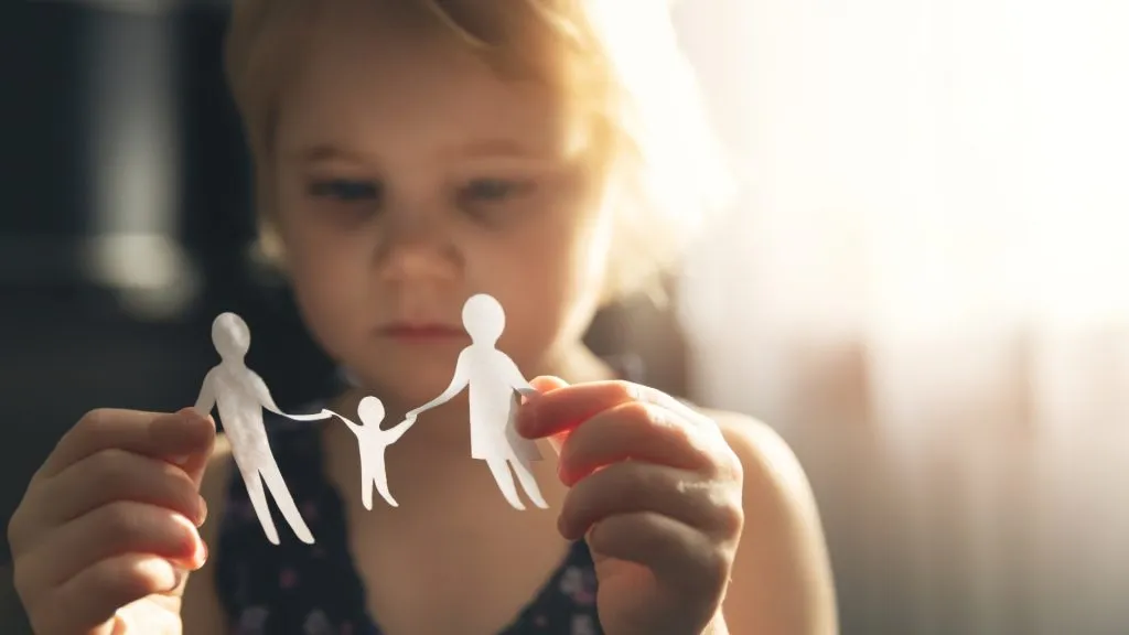 A young child holding paper cutouts of a family, symbolizing separation or child custody.