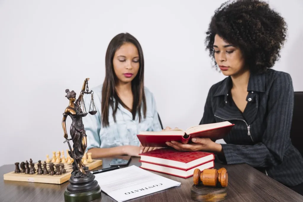 An image of an African American woman pointing out something in a book to another girl.