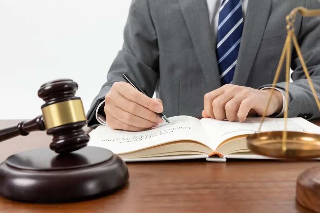 An image of a close up shot person that writing on his book with the gavel and justice scale on the table