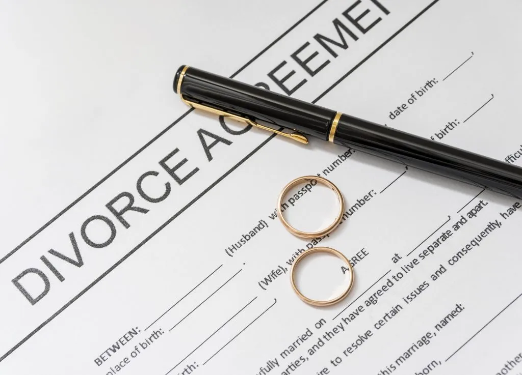 An image of a divorce agreement, a pen, and a pair of wedding rings.