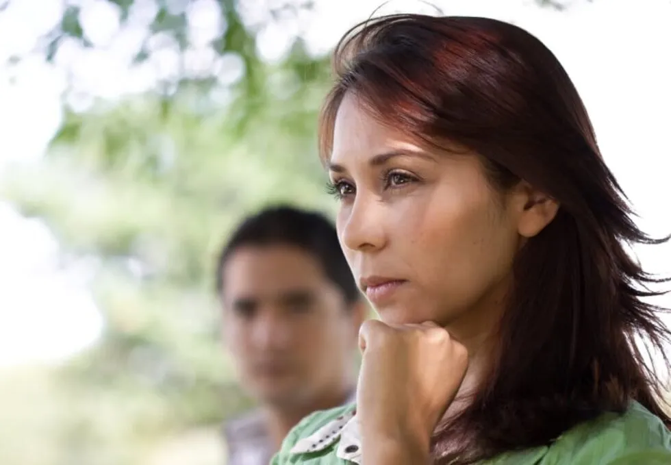 An image of a woman staring into the distance, deep in thought about divorce. And a man in the blurry background.