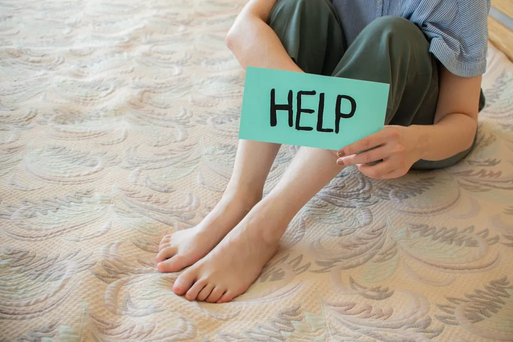 An image of a person affected by human rights abuses, holding a paper with the word “HELP” written on it.