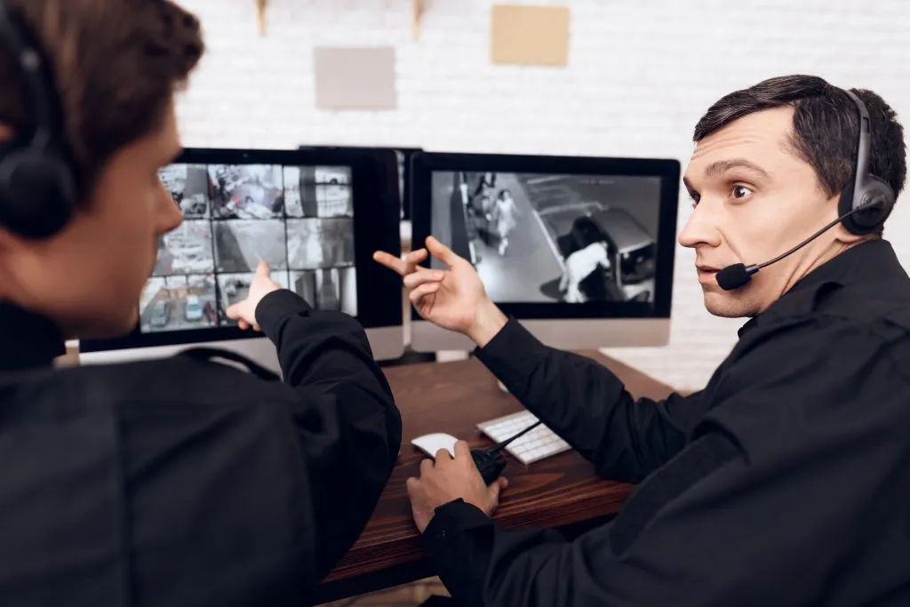 An image of two people sitting in front of a monitor, watching and monitoring CCTV footage