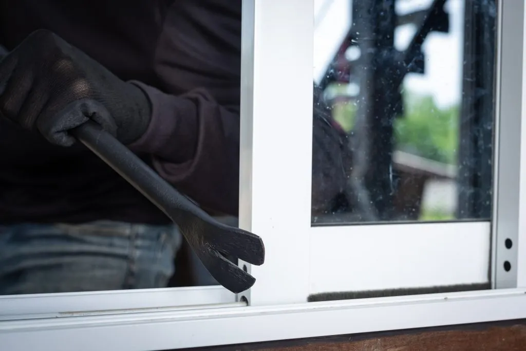 An image of thieves wearing black gloves and jackets, holding an object to pry open a window.