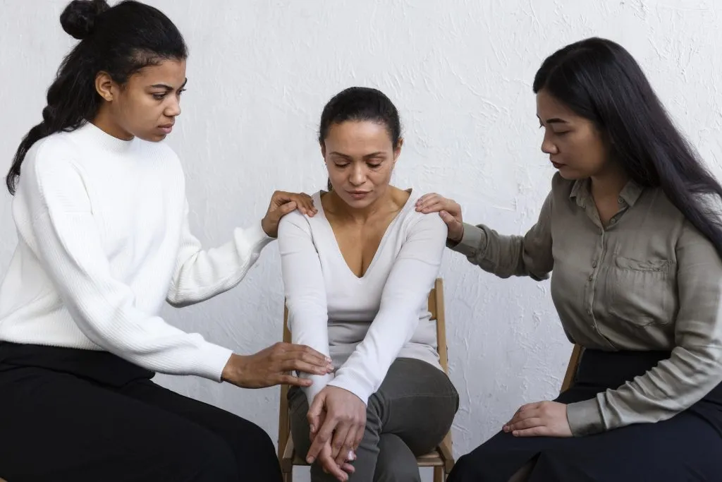 An image of a sad woman looking distressed, being comforted by two other women.