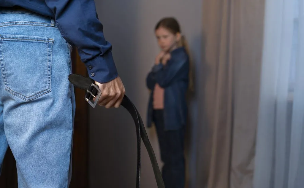 An image of a young girl in distress, facing abuse as her father raises a belt.